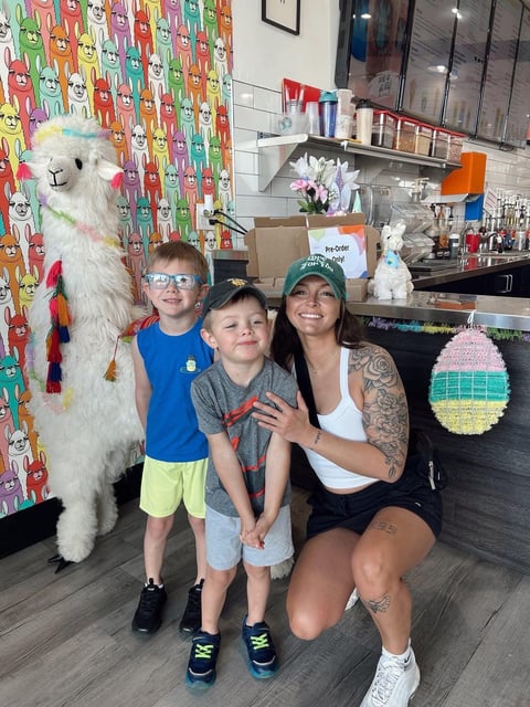 Adult and two children posing with a large white alpaca in a colorful kitchen decorated with animal illustrations